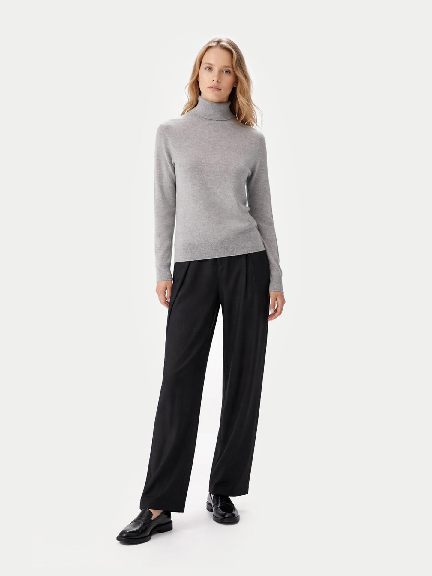 Vue de face d'une femme portant un pull à col roulé gris et un pantalon noir sur fond gris clair. #color_high-rise