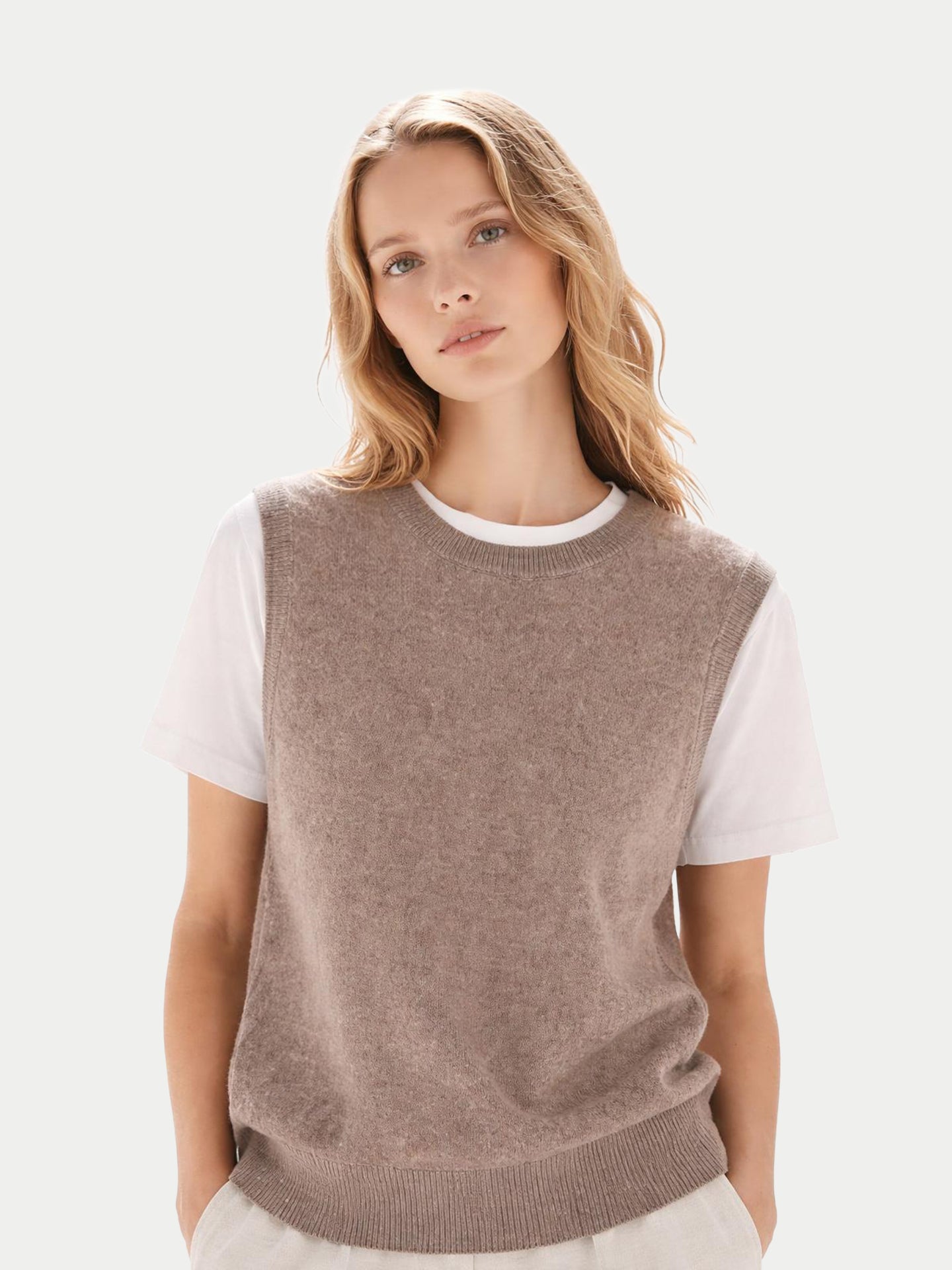 Gros plan de face d'une femme portant un débardeur beige à col rond sur un t-shirt blanc, sur fond gris clair. #color_taupe