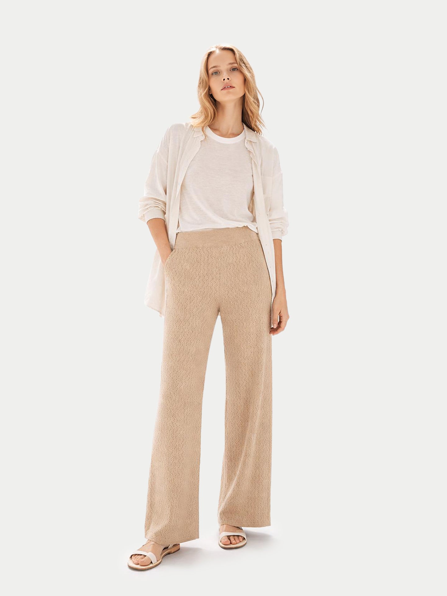 Vue de face d'une femme portant une chemise blanche sur un t-shirt et un pantalon large beige en maille côtelée, sur fond gris clair. #color_beige