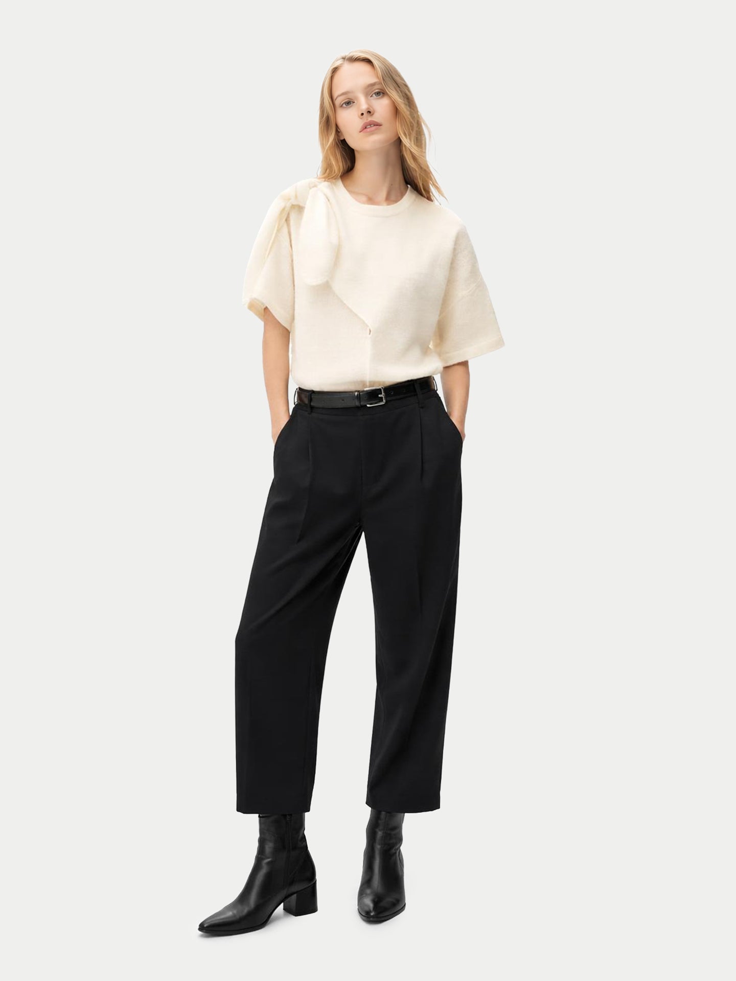 Vue de face d'une femme portant un haut en cachemire blanc à manches courtes et col rond, avec une écharpe nouée sur l'épaule et un pantalon noir, sur fond gris clair. #color_blanc