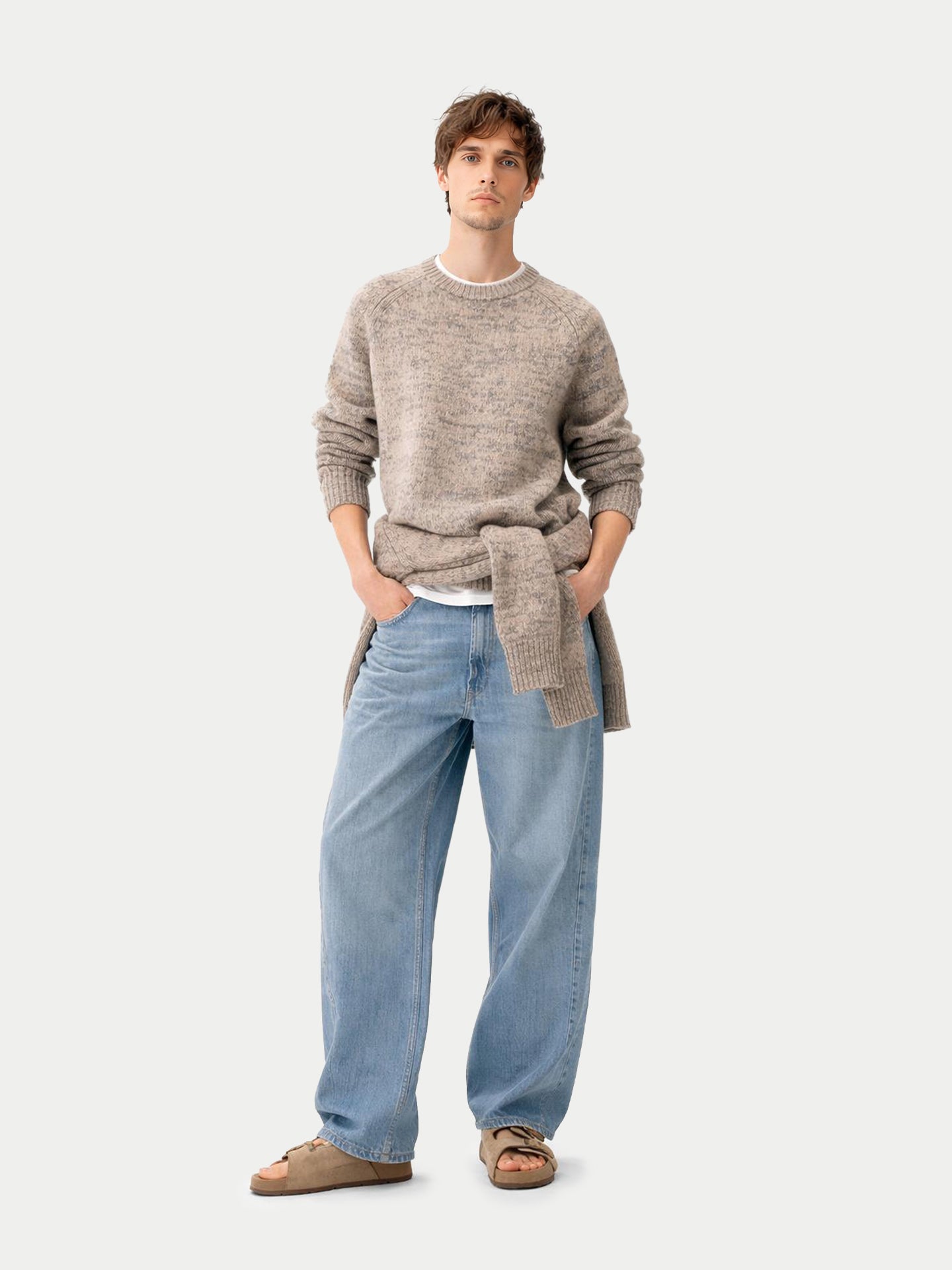 Vue de face d'un homme debout, portant un pull ras du cou beige-taupe noué à la taille, par-dessus un jean bleu, sur fond gris clair. #color_oxfor-tan